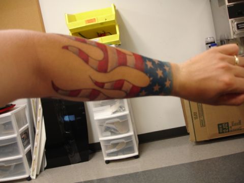 1986 Ford Bronco - Tattoo of the American flag with flames wraps around an arm, with a Supermotors logo in the corner.