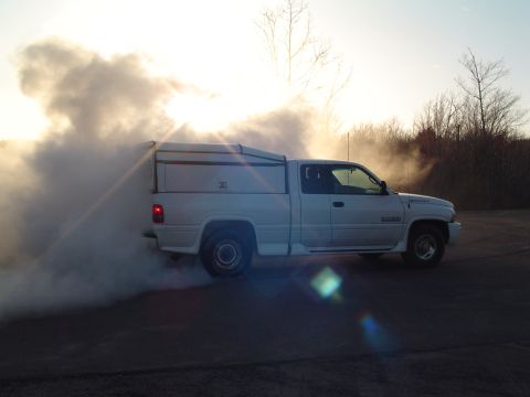 2000 Chevrolet Tahoe - A white pickup truck performs a burnout, creating a large cloud of smoke against the setting sun.