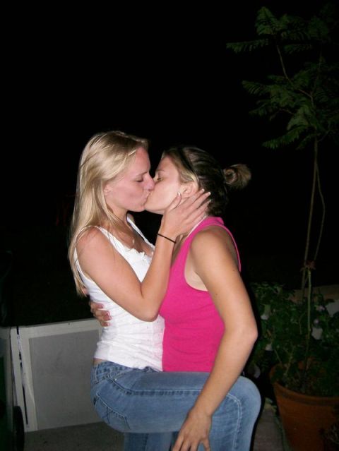 1989 Ford Bronco - Two women share a kiss in front of a dark background with some foliage.