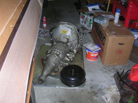 1975 Ford Ranchero - A transmission and torque converter are laid out on a drip pan in a garage setting.