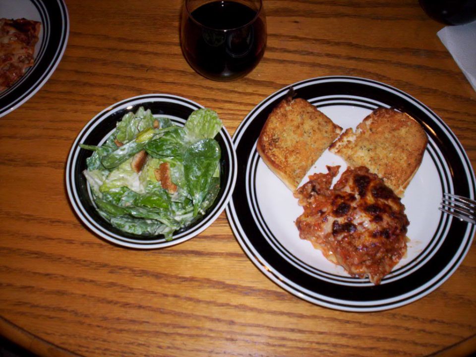 Plate of lasagna with garlic toast and a side salad with a glass of red wine