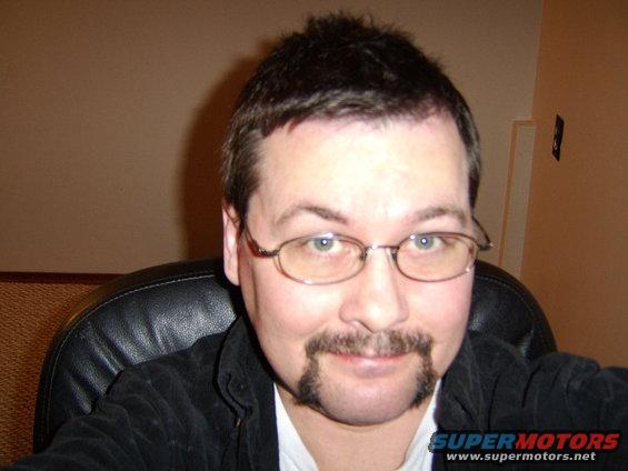 Man with glasses and mustache, Supermotors logo visible