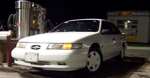 1993 Ford Taurus - A white sedan is parked at a gas station with vacuum cleaners in the background.