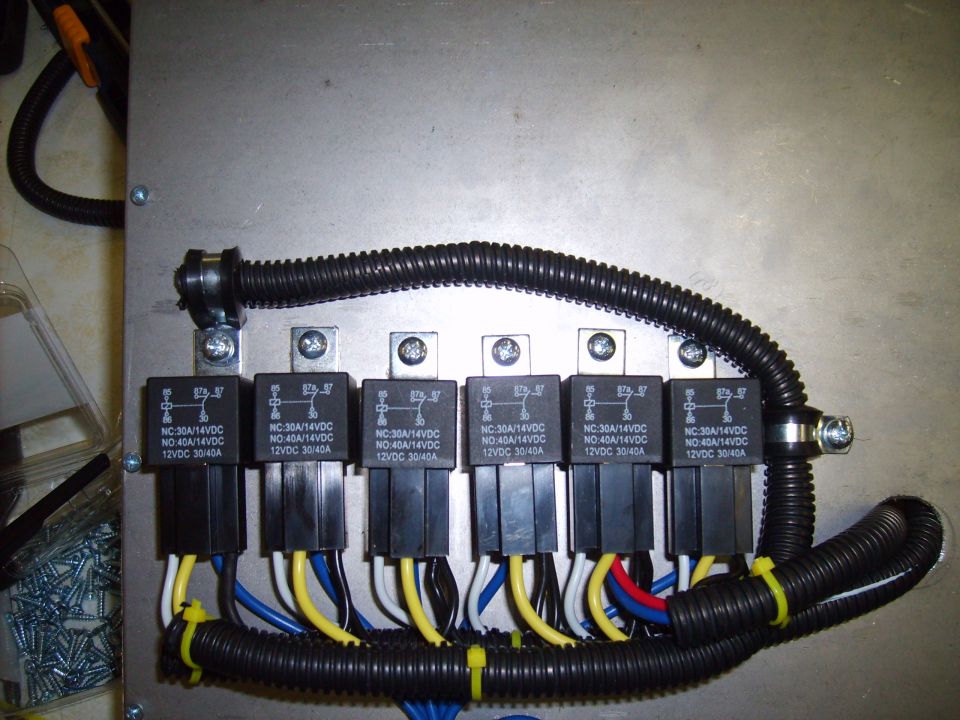 Close-up of a wiring harness with multiple automotive relays and black protective conduit