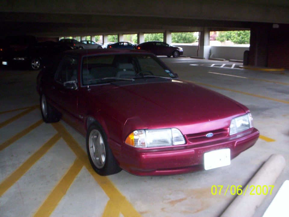 Maroon Ford Mustang hatchback parked in a concrete parking garage, front three-quarter view.