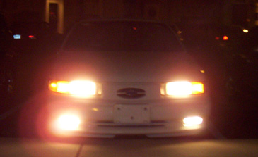 1993 Ford Taurus - The front of a white car is visible at night, with its headlights on.