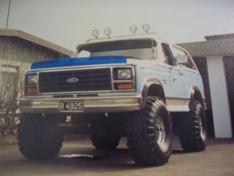 1996 Ford Bronco - This lifted SUV features oversized tires, roof-mounted lights, and a distinctive blue hood accent. The license plate reads R 4925.