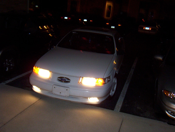 1993 Ford Taurus parked at night, headlights on. Another car is visible to the right