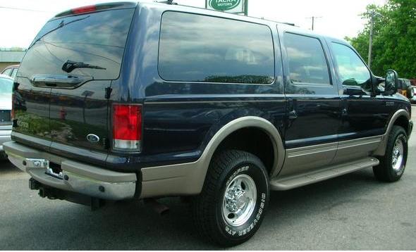 Dark blue Ford SUV rear three-quarter view with tan cladding and chrome wheels in a lot