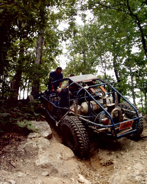 1989 Ford Bronco II - An off-road buggy navigates a challenging rocky trail surrounded by trees.