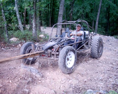 1989 Ford Bronco II - A man drives a custom-built off-road buggy through a wooded area, with a tow strap attached to the front.