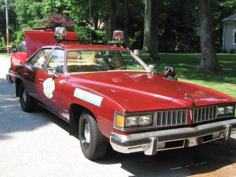 1991 Ford Crown Victoria - A vintage red police car with emergency lights and official markings is parked on a street.