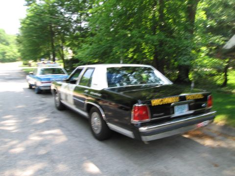 1991 Ford Crown Victoria - Two police cars are parked on a residential street, one in the foreground and another behind it.