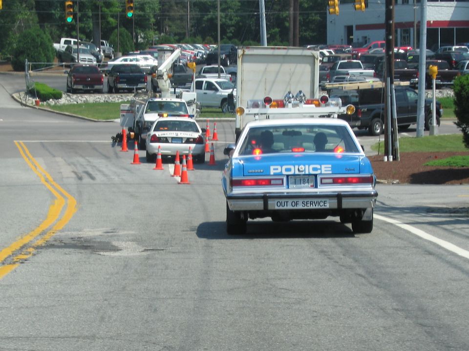 Rear of blue POLICE sedan with OUT OF SERVICE plate driving on a road