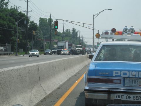 1991 Ford LTD Crown Victoria - blue Dodge POLICE sedan with a roof light bar stopped at a green-lit intersection beside a concrete highway barrier.