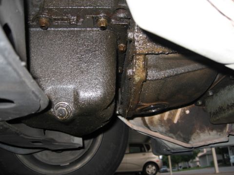 1995 Mercury Cougar - The underside of a vehicle's engine and transmission is covered in oil, with another car visible in the background.