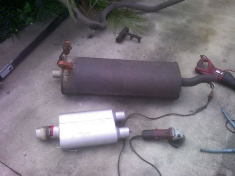 2001 Ford F-150 - Two exhaust mufflers, one old and one new, are shown on a concrete surface with power tools nearby.