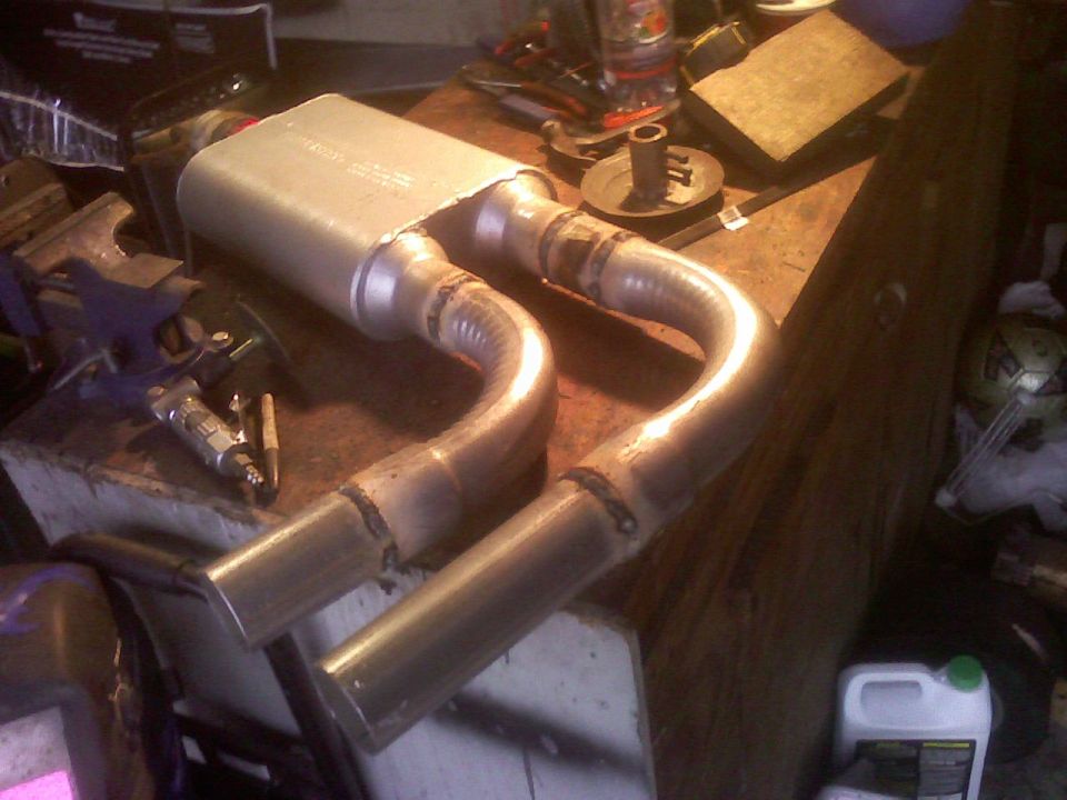 Fabricated dual exhaust with welded U-bends and angle-cut tips on a workbench