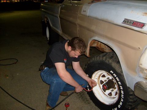 1976 Ford F-100 - A man is shown inflating the tire of a lifted pickup truck. The truck appears to be a Ford F-Series from the mid-1970s.