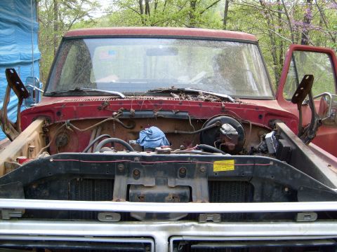 1976 Ford F-100 - The engine bay of a red Ford truck is visible with the hood open, revealing engine parts and a blue cloth.
