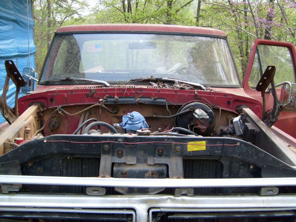 Red Ford truck engine bay with hood open, showing engine components and a blue cloth. Grille reads "FORD"