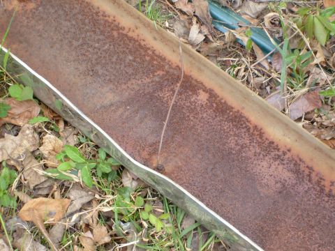 1976 Ford F-100 - A heavily rusted metal pipe lies on the ground, showing signs of damage and decay.