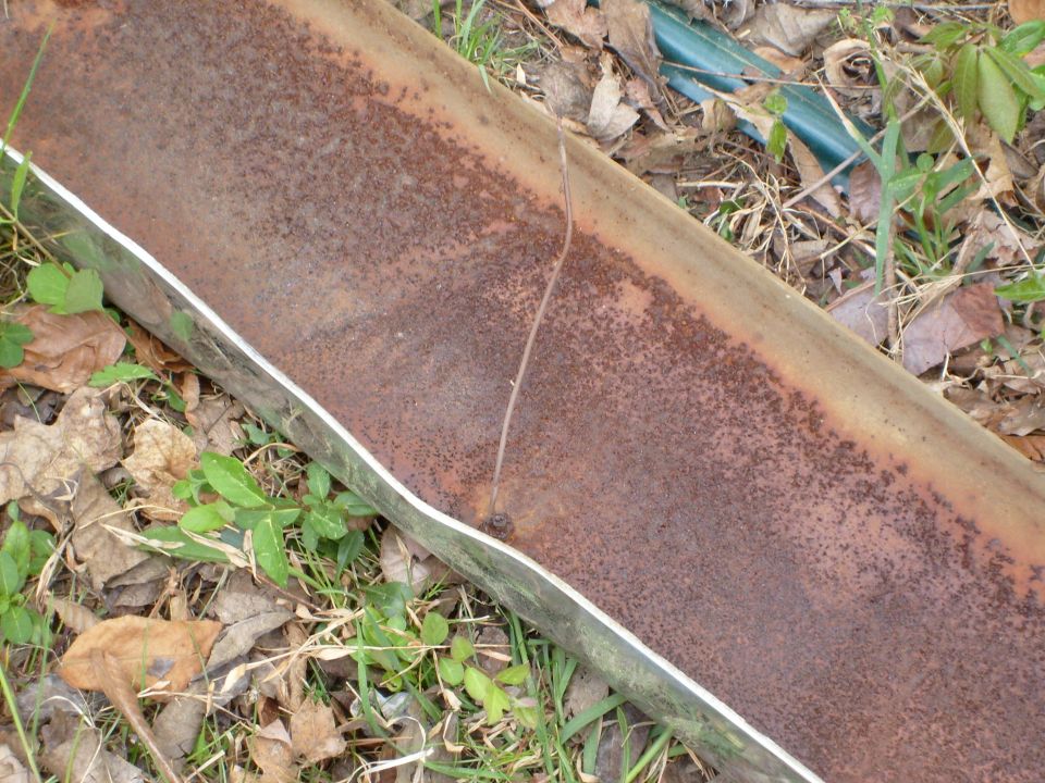 rusted metal pipe with a crack, lying on the ground with leaves and grass