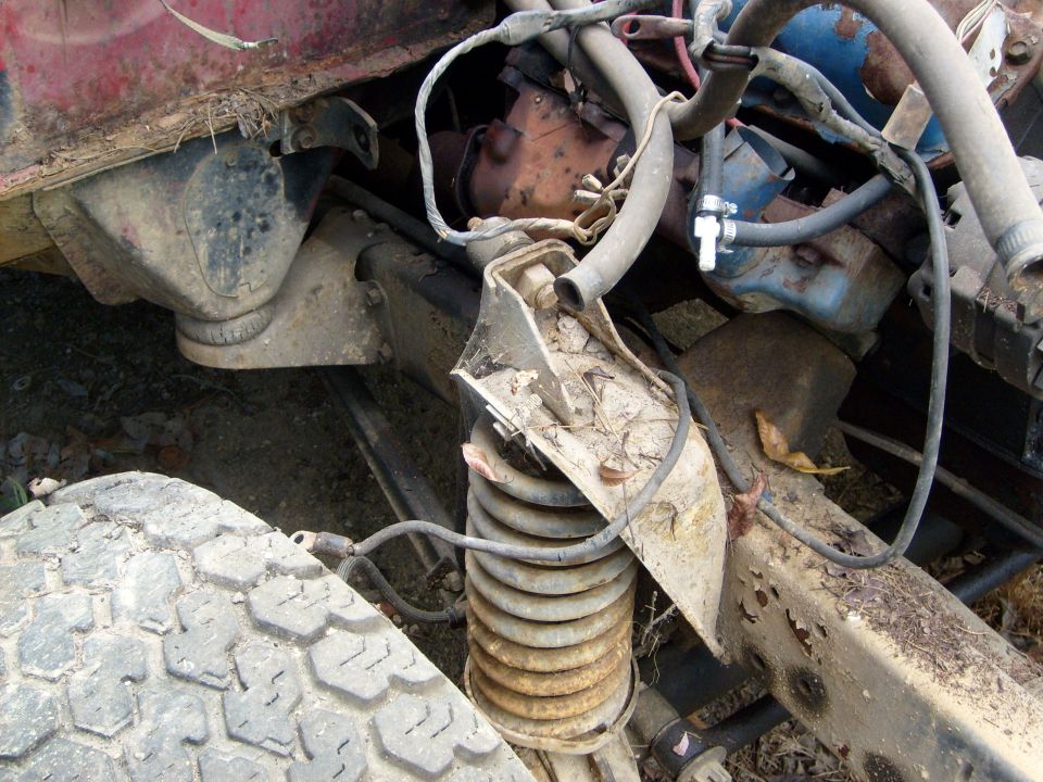 Engine and suspension parts of a rusty vehicle, showing a coil spring and hoses