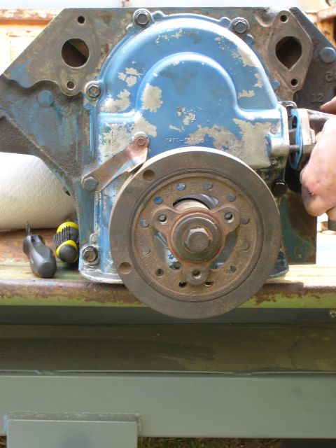 1976 Ford F-100 - Close-up of an engine timing cover and pulley assembly, with a hand visible on the right.