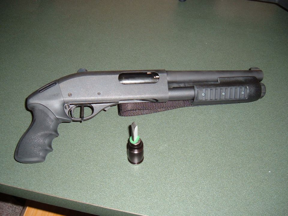 Black pump-action shotgun with a sling and a green-tipped cartridge on a green surface