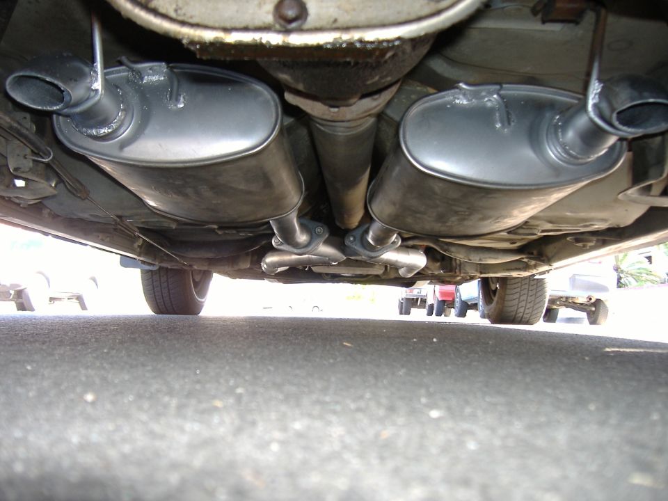 Underbody view of dual exhaust with two mufflers and clamped pipes beneath a car over asphalt