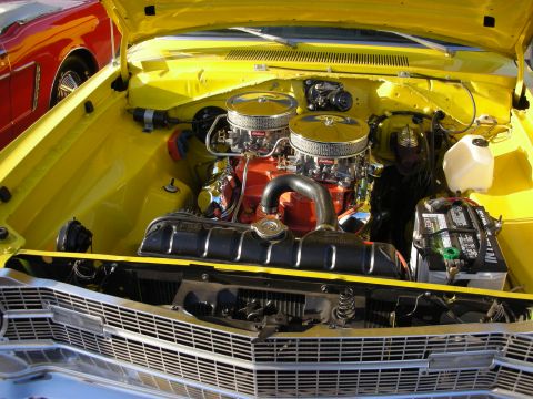 1998 Ford Crown Victoria - The engine bay of a yellow car features dual carburetors and chrome air cleaners, with a red vehicle partially visible on the left.