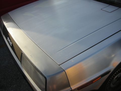 1998 Ford Crown Victoria - The front corner of a silver DeLorean DMC-12 is visible, showing the distinctive grille and headlight assembly.