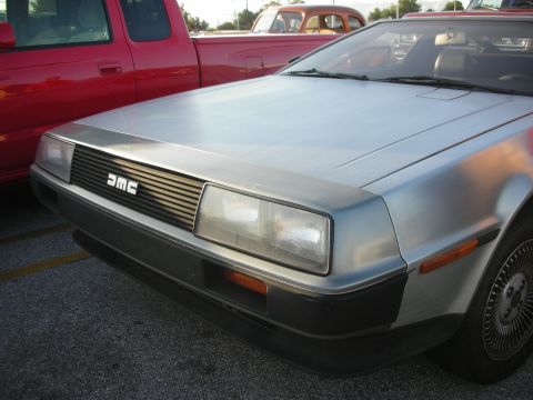 1998 Ford Crown Victoria - A silver DMC DeLorean is parked next to a red pickup truck, with another car in the background.