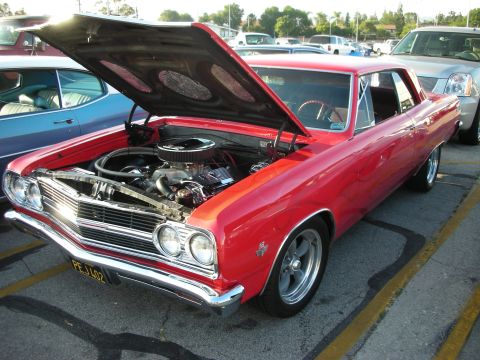 1998 Ford Crown Victoria - A red 1966 Chevrolet Chevelle coupe is parked with its hood open, revealing the engine and aftermarket wheels.