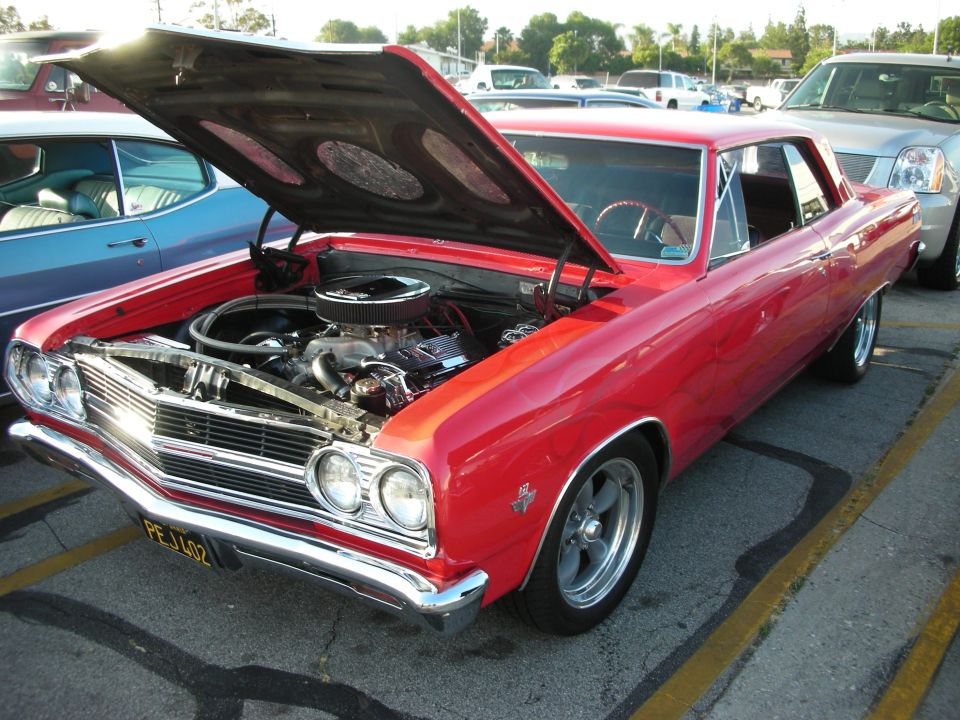 Red 1966 Chevrolet Chevelle coupe with hood open, showing engine. Chrome grille and bumper. Aftermarket wheels