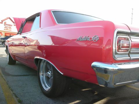 1998 Ford Crown Victoria - A red 1960s Chevrolet Malibu SS coupe is seen from the rear quarter angle, with its hood open.