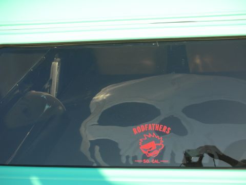 1998 Ford Crown Victoria - A skull graphic and a Rodfathers So. Cal sticker are visible on the tinted window of a teal-colored vehicle.
