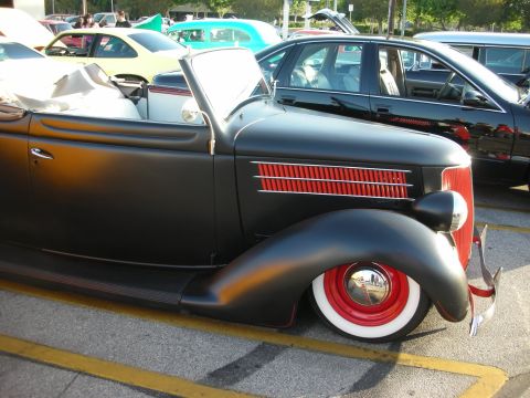 1998 Ford Crown Victoria - A classic black convertible with distinctive red accents on the grille and wheels is parked in a lot with other vehicles.