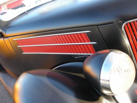 1998 Ford Crown Victoria - Close-up of a vintage black car's fender, red louvers and a prominent chrome headlight.