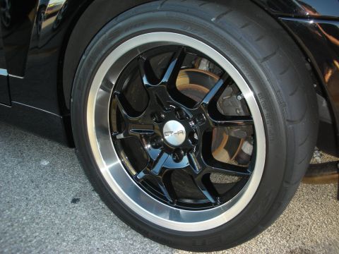 1998 Ford Crown Victoria - A close-up view of a custom wheel and tire on a black vehicle, showing the intricate spoke design and a branded center cap.