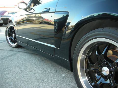 1998 Ford Crown Victoria - A black car is viewed from the side, highlighting its custom wheels and reflective paintwork.