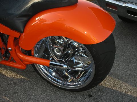 1998 Ford Crown Victoria - Close-up of a custom motorcycle's rear wheel and orange fender, with another vehicle visible.