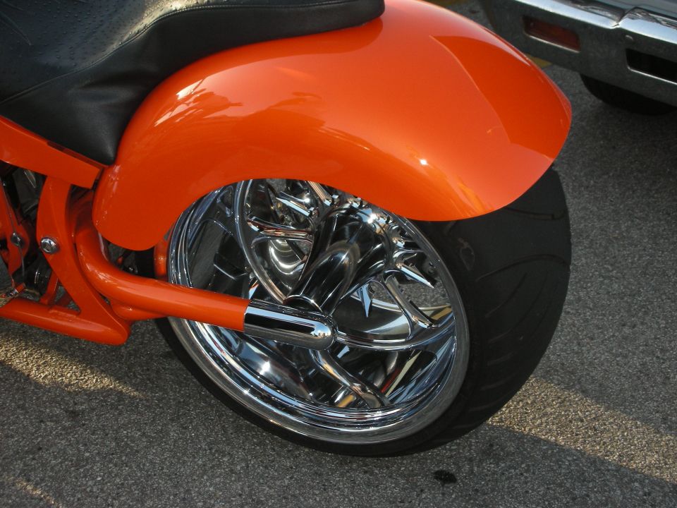 Orange motorcycle rear fender and chrome wheel with a car in the background