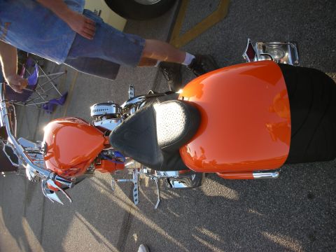 1998 Ford Crown Victoria - A custom motorcycle with bright orange bodywork and a black seat is parked outdoors.