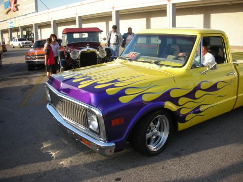 1998 Ford Crown Victoria - A yellow pickup truck with custom flame paint is parked next to other vehicles.