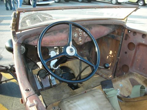 1998 Ford Crown Victoria - The interior of a weathered, classic car shows a large steering wheel, exposed metal, and a wooden floor.