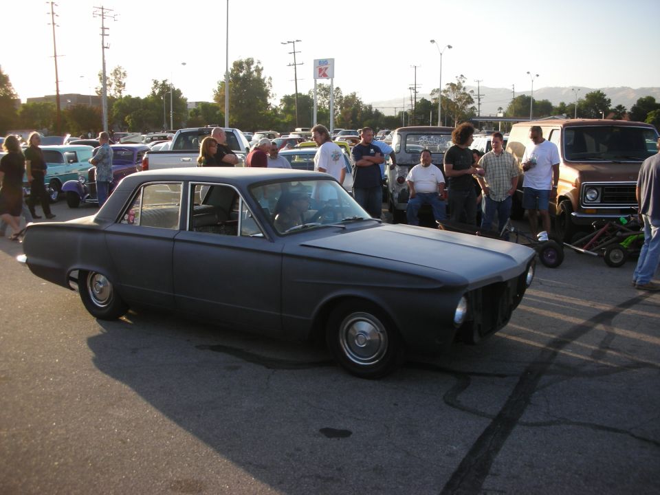 Dark matte sedan with a missing grille, viewed from the front three-quarter angle