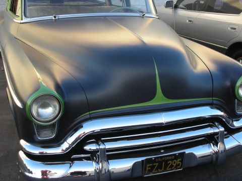 1998 Ford Crown Victoria - A matte black hot rod with green pinstriping and a chrome grille is parked next to another vehicle.
