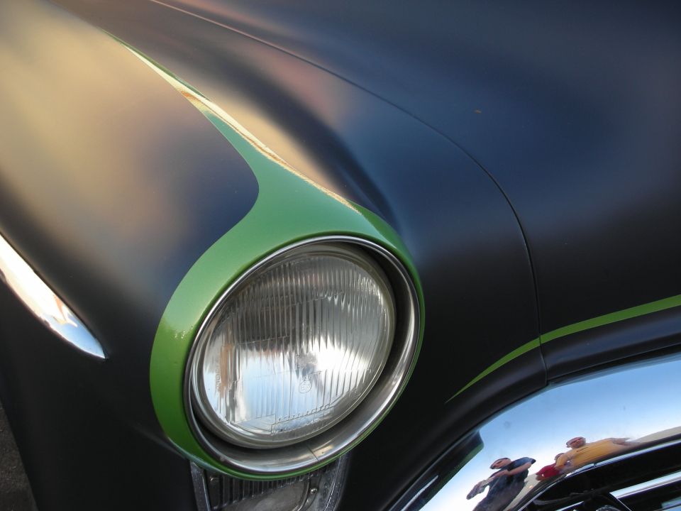 Close-up of a car's headlight with a matte black finish and a green flame graphic. Chrome trim is visible